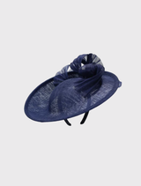 Navy blue Yumi fascinator with a curving design on a circular base, elegantly fitted on a headband for race day attire.