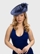 Navy blue Yumi fascinator with swirling ribbon trim on a circular base, secured on a sleek headband for formal occasions.