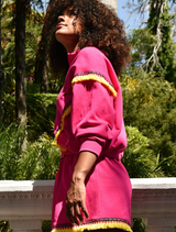 A woman with an afro in a pink sweatsuit poses, reflecting a blend of comfort and contemporary fashion.