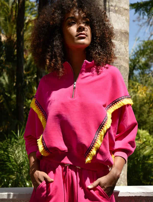 A woman with an afro wearing a pink sweatsuit stands confidently, showcasing her vibrant style and personality.