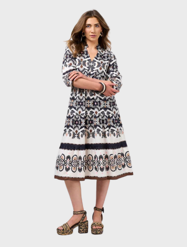 A woman wearing a dress adorned with an intricate, ornate pattern, standing gracefully against a neutral background.